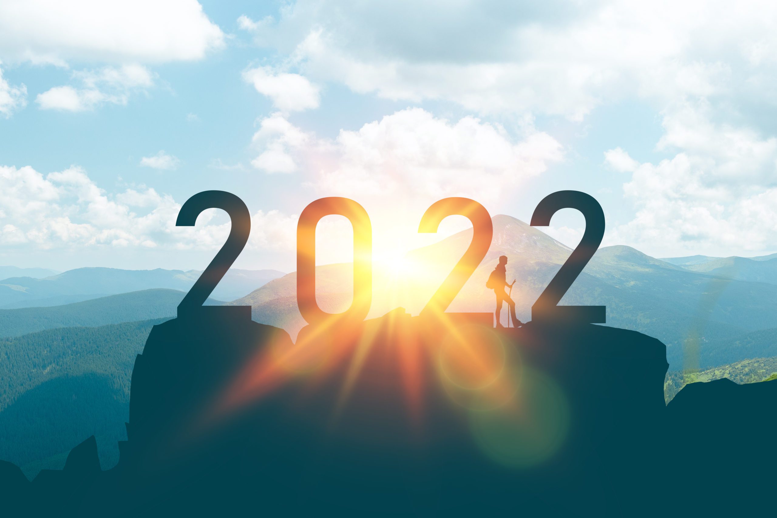 the silhouette of the number 2022 on a mountain top as the sun rises behind and a man stands nearby